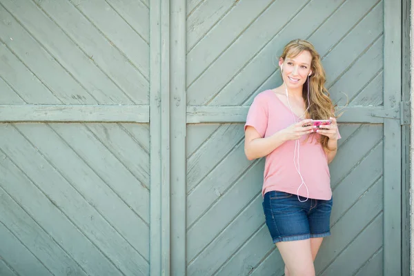 Porträt einer jungen erwachsenen Frau mit braunen Augen, die mit Kopfhörern auf ihrem Smartphone Musik hört. — Stockfoto