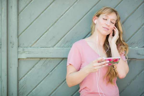 Retrato al aire libre de una mujer joven de ojos marrones escuchando música con auriculares en su teléfono inteligente . —  Fotos de Stock