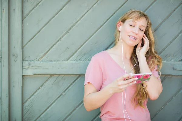 Kültéri álló fiatal felnőtt barna szemű nő hallgató-hoz zene-val fülhallgató ő okos telefon. — Stock Fotó