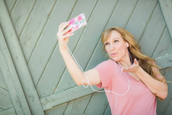 Ung vuxen kvinna som bär hörlurar tar en Selfie med sin smarta telefon. — Stockfoto