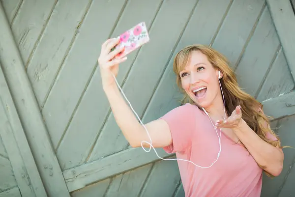 Mujer joven adulta usando auriculares tomando una selfie con su teléfono inteligente . —  Fotos de Stock