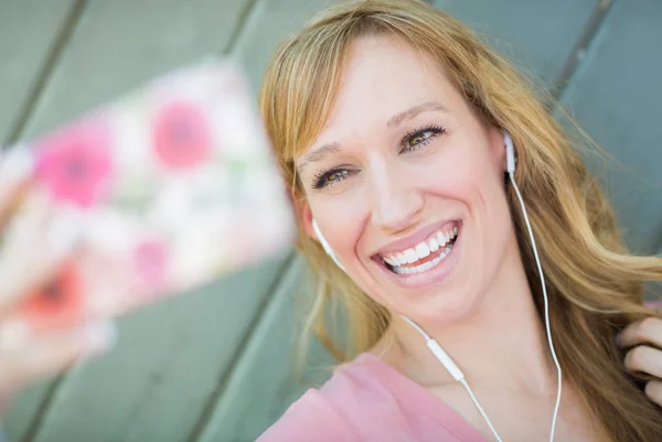 Jeune femme adulte portant des écouteurs prenant un selfie avec son téléphone intelligent . — Photo