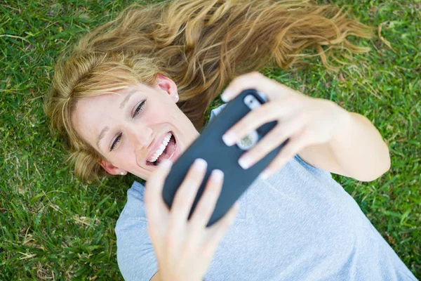 Genç yetişkin kadın onun akıllı telefon ile bir Selfie alarak çim döşeme. — Stok fotoğraf