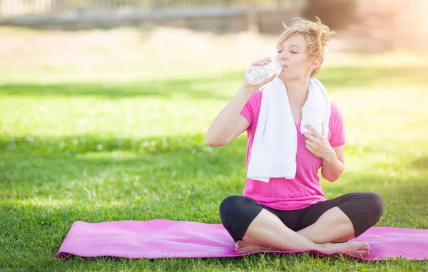 Jeune femme adulte en plein air sur son tapis de yoga avec serviette Drinki — Photo