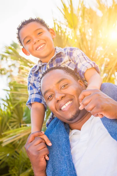 Zoon van gemengd ras en Afrikaanse Amerikaanse vader samenspelen Piggyback buitenshuis. — Stockfoto