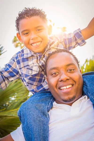 Zoon van gemengd ras en Afrikaanse Amerikaanse vader samenspelen Piggyback buitenshuis. — Stockfoto