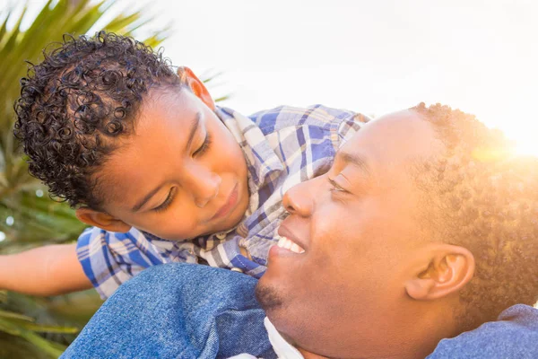Zoon van gemengd ras en Afrikaanse Amerikaanse vader samenspelen Piggyback buitenshuis. — Stockfoto