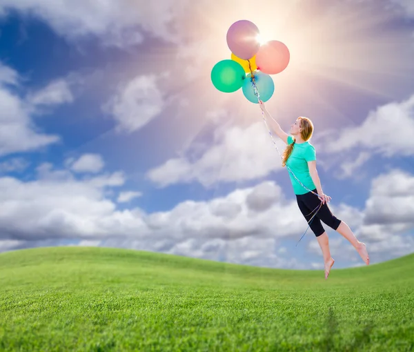 Jovencita siendo llevada arriba y lejos por globos que ella está sosteniendo por encima del campo de hierba por debajo . — Foto de Stock