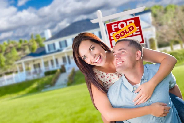 在与出售的房地产标志的家门前嬉戏兴奋军事夫妇. — 图库照片