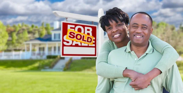 Szczęśliwy African American para naprzeciwko pięknego domu i sprzedane sprzedaż nieruchomości znak. — Zdjęcie stockowe