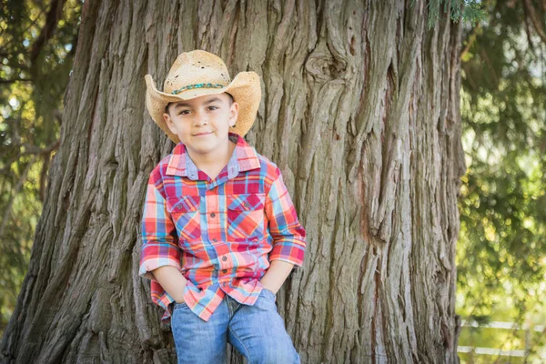 Misto raça jovem menino vestindo vaqueiro chapéu de pé ao ar livre . — Fotografia de Stock