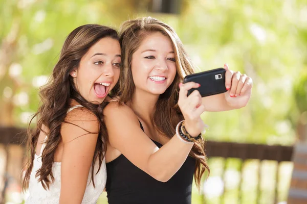 Zwei attraktive gemischte Rassenfreundinnen, die ihr Smartphone für ein Selfie im Freien benutzen — Stockfoto