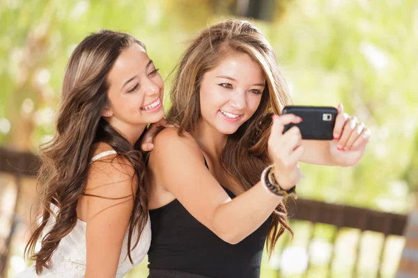 Due attraenti fidanzate di razza mista che usano i loro telefoni cellulari intelligenti per selfie all'aperto — Foto Stock
