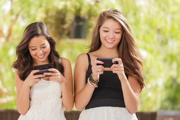 Twee vriendinnen van de expressieve gemengd ras met behulp van hun slimme mobiele telefoons buitenshuis — Stockfoto