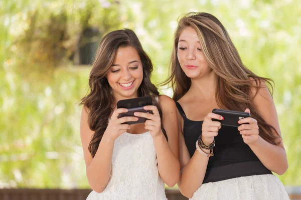 Duas expressivas namoradas de raça mista usando seus telefones celulares inteligentes ao ar livre — Fotografia de Stock