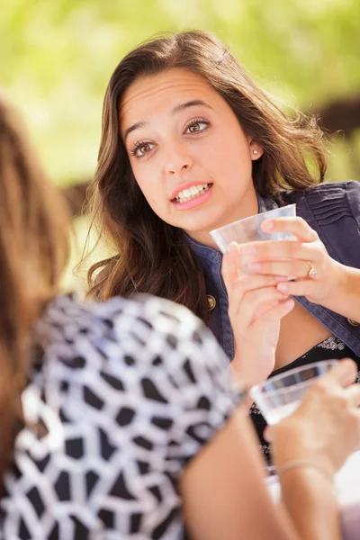 表現力豊かな若い大人の女性の飲み物を持つと彼女の友人の屋外で話して — ストック写真