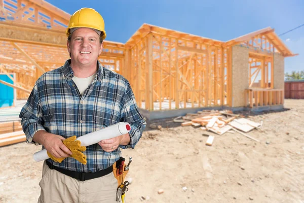 Contratista masculino con los planes de la casa que usa el sombrero duro delante del marco de la construcción de la casa nueva — Foto de Stock