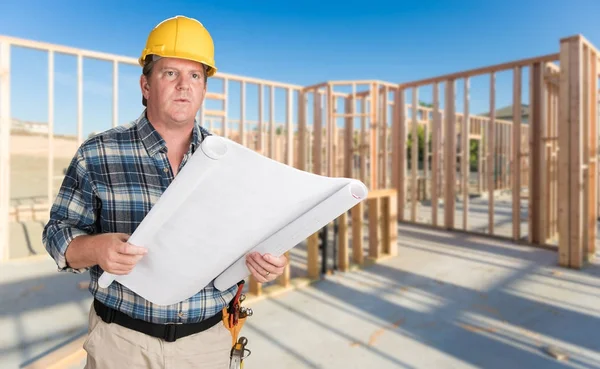 Empreiteiro masculino com planos de casa vestindo chapéu duro dentro da construção da nova casa — Fotografia de Stock