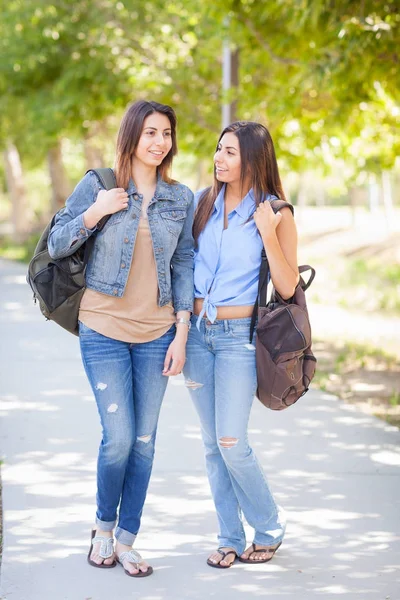Dos hermosas hermanas gemelas étnicas jóvenes con mochilas caminando al aire libre . — Foto de Stock