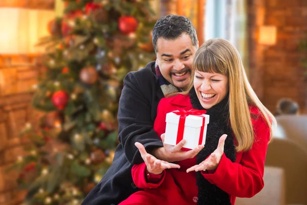 Gemischtes Paar teilt Weihnachten vor geschmücktem Baum. — Stockfoto