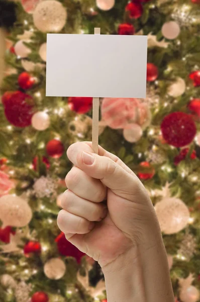 Χέρι που κρατά κενή κάρτα μπροστά από το στολισμένο χριστουγεννιάτικο δέντρο. — Φωτογραφία Αρχείου