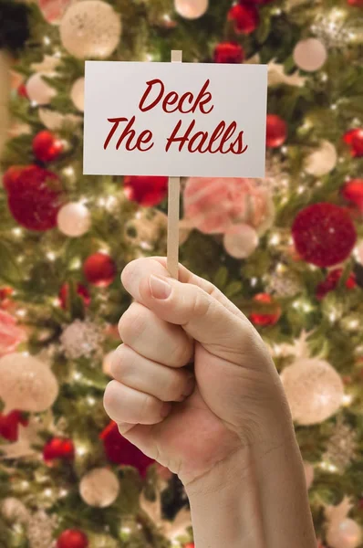 デッキに飾られたクリスマス ツリーの前でホールのカードを持っている手. — ストック写真