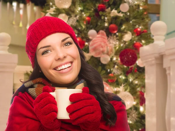 Warm gekleidete Frau mit Becher vor geschmücktem Weihnachtsbaum. — Stockfoto