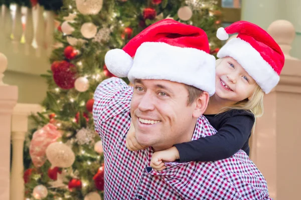 Vater und Tochter mit Weihnachtsmützen vor geschmücktem Weihnachtsbaum. — Stockfoto