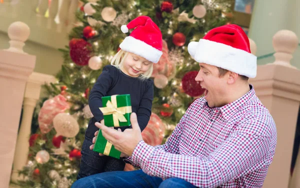 Gelukkig jong meisje en vader dragen van Santa hoeden doos van de Gift voor versierde kerstboom. — Stockfoto