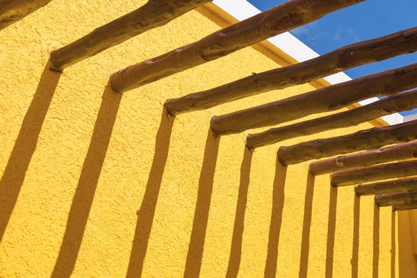 Vigas de poste de madera abstractas y pared amarilla brillante contra el cielo azul —  Fotos de Stock