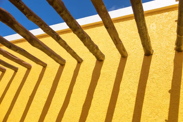 Vigas de poste de madera abstractas y pared amarilla brillante contra el cielo azul —  Fotos de Stock