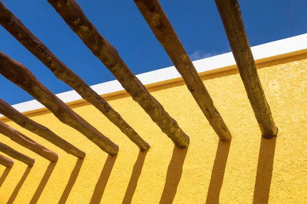 Abstrakta trästolpe balkar och ljusa gula vägg mot blå himmel — Stockfoto