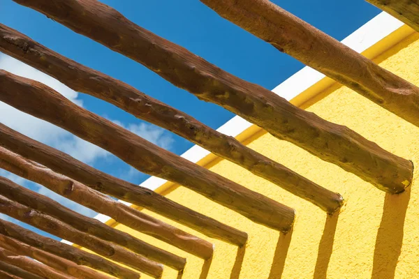 Vigas de poste de madera abstractas y pared amarilla brillante contra el cielo azul — Foto de Stock