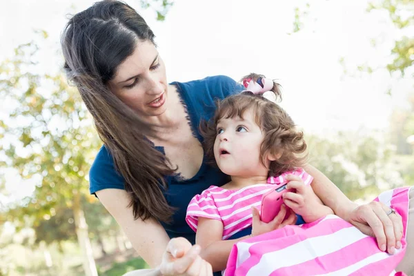 Madre de raza mixta y linda hija bebé jugando con el teléfono celular en el parque . — Foto de Stock