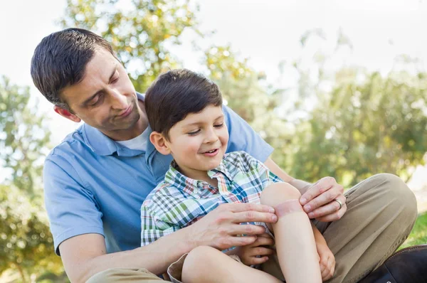 Kärleksfull Fader sätter ett bandage på armbåga av sin unga son i parken. — Stockfoto