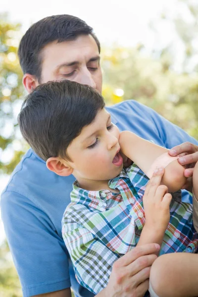 Liefdevolle vader zet een pleister op de elleboog van zijn jonge zoon in het park. — Stockfoto
