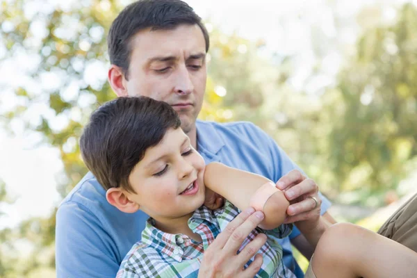 Στοργικός πατέρας βάζει έναν επίδεσμο στο αγκώνα του γιό του στο πάρκο. — Φωτογραφία Αρχείου