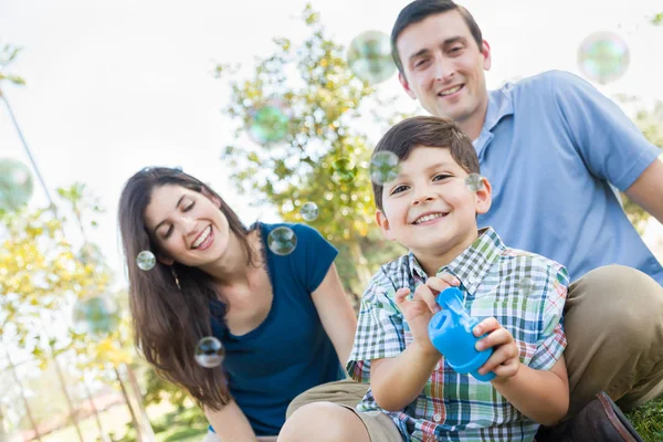 Ung pojke blåsa bubblor med sina föräldrar i parken. — Stockfoto