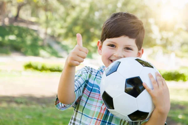 Schattige jonge jongen met voetbal en duimen omhoog buiten spelen in het Park. — Stockfoto