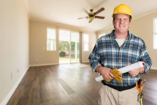 Entrepreneur avec des plans et un casque à l'intérieur chambre vide avec planchers de bois . — Photo