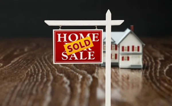 Sprzedany za sprzedaż nieruchomości znak przed domem Model na odblaskowej powierzchni drewnianych. — Zdjęcie stockowe