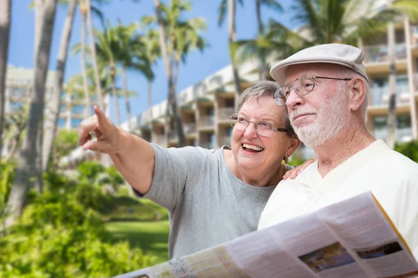 Felices turistas adultos mayores con folleto al lado de hotel tropical y palmeras . —  Fotos de Stock