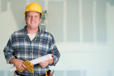 Contractor with Plans and Hard Hat In Front of Drywall. clipart