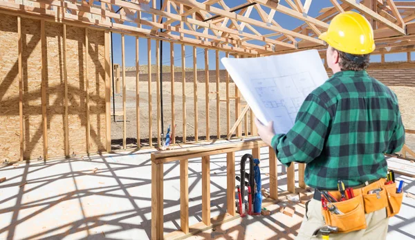 Contratista con casco duro y planes de pie dentro del marco de construcción de la nueva casa . — Foto de Stock