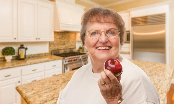 Heureuse femme adulte âgée avec pomme rouge à l'intérieur de la cuisine . — Photo