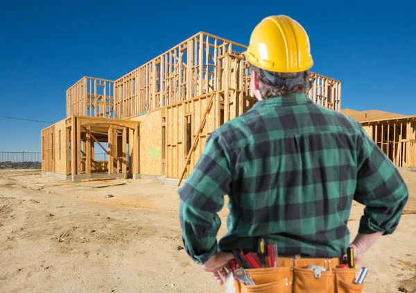 Contratista con casco duro mirando el nuevo marco de la casa en el sitio de construcción . — Foto de Stock