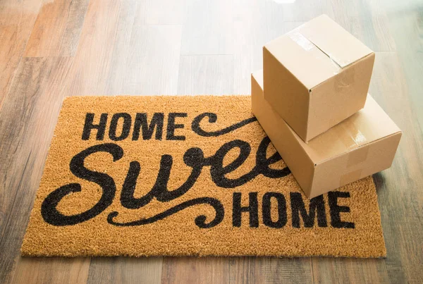 Home Sweet Home Alfombra de bienvenida en piso de madera con envío de cajas . — Foto de Stock