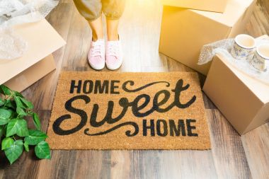 Kadın pembe Ayakkabı ve Home Sweet Home hoş geldiniz Mat, kutular ve bitki ayakta terleme.