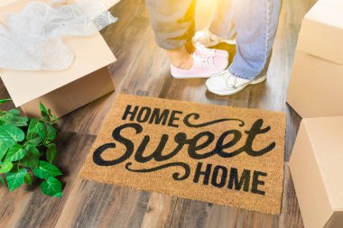 Man and Woman Standing Near Home Sweet Home Welcome Mat, Moving Boxes and Plant. clipart