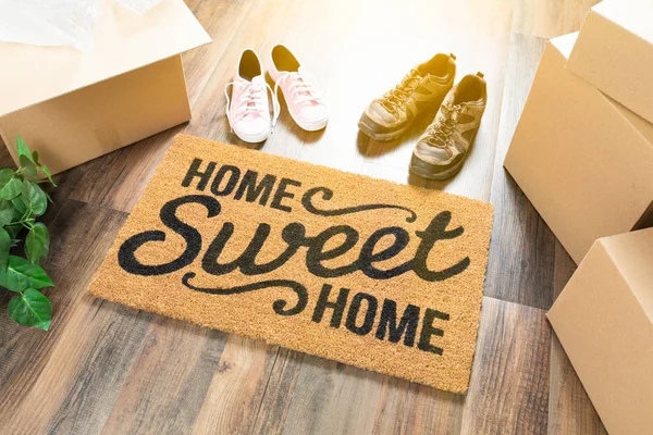 Home Sweet Home Esterilla de bienvenida, cajas móviles, zapatos para hombres y mujeres y plantas en pisos de madera dura . — Foto de Stock